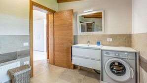Een kleine badkamer met een houten deur, een wastafel, een spiegel, een wasmachine en een betegelde vloer.