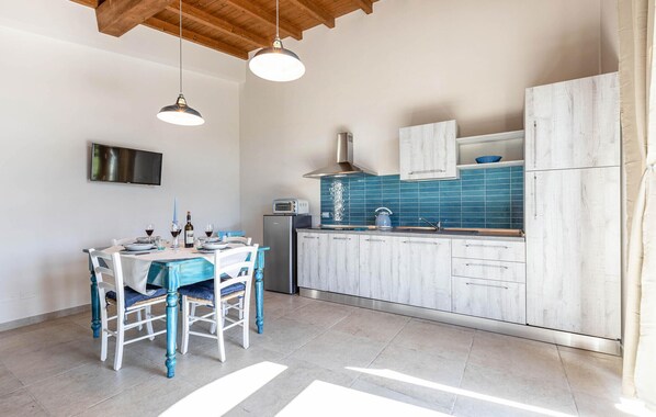 Una cocina moderna con armarios blancos, salpicadero de azulejos azules y un comedor con mesa y sillas.