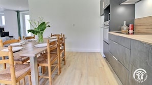 Een moderne keuken met een houten eettafel gedekt voor vier personen, een ingebouwde oven en een aanrecht met een blikje bier.