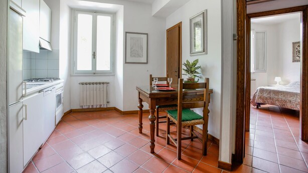 A kitchen with white cabinets, a stove, and a window. There is a dining table with chairs and a potted plant. - Nice apartment in Firenze with WiFi (Firenze)