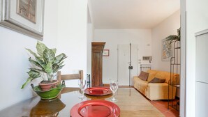 A dining area with a wooden table set for two, a green potted plant, and a sofa in the background. - Nice apartment in Firenze with WiFi (Firenze)