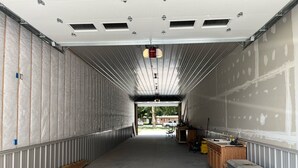 A large, empty warehouse with a high ceiling and metal walls, featuring a long, narrow aisle and a small workbench with tools. - Fisherman's Retreat! (Burwell)