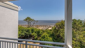 Een balkon met uitzicht op de zee, een houten looppad en weelderige begroeiing.