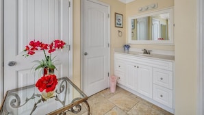 Een badkamer met witte meubels, een wastafel met spiegel en een glazen tafel met een bloemenvaas.