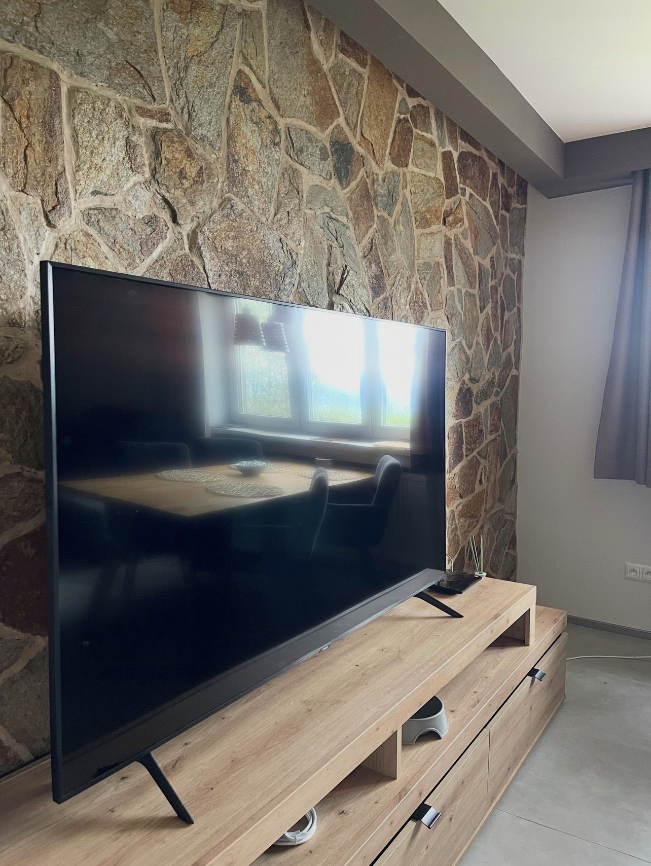 A flat-screen TV on a wooden TV stand against a stone wall.