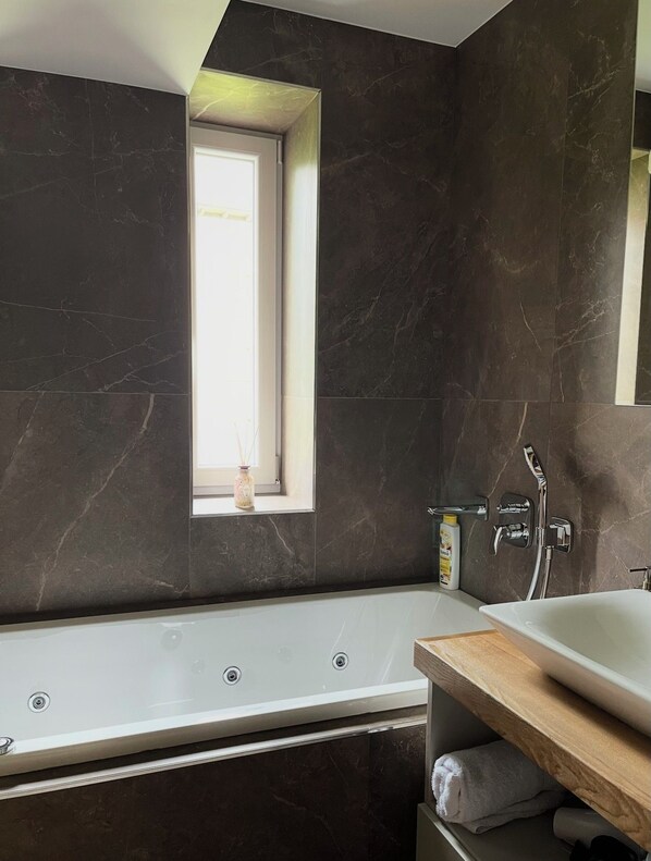 A modern bathroom with a bathtub, a window, and a shower area.