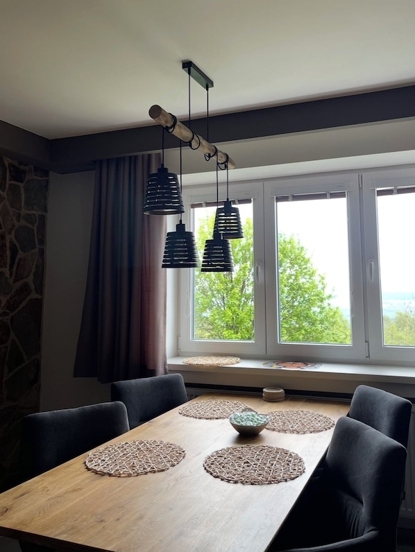 A dining area with a wooden table, black chairs, woven placemats, and pendant lights. - Luxury apartment with sauna - family and pet friendly (Vysoké Tatry)