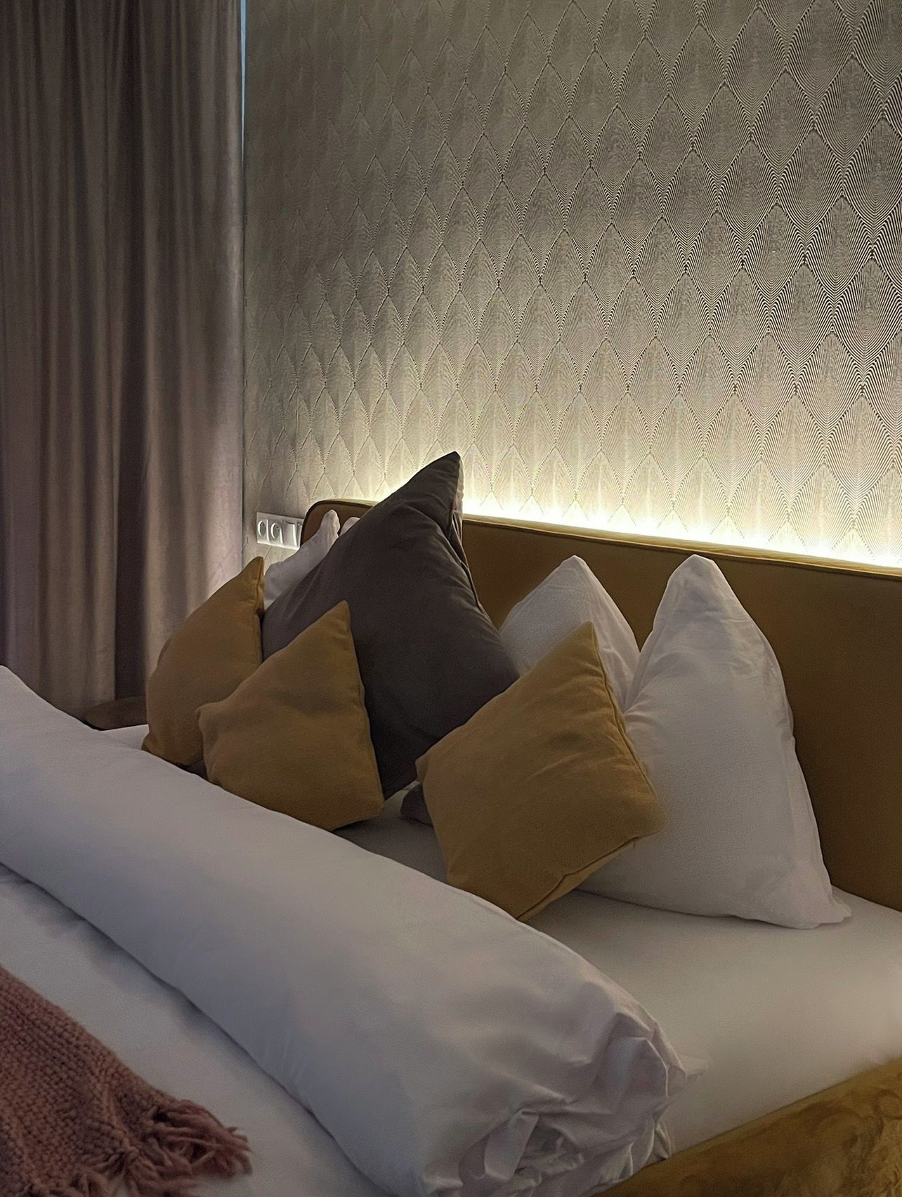 A hotel room with a bed, pillows, and a wall with a textured pattern.