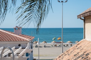 A beach view with a building, palm trees, and a clear sky.