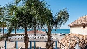 Une vue sur la plage, avec des palmiers, une pergola et un bâtiment doté d’un toit en tuiles.
