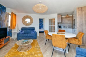 Una sala de estar moderna con sofá, mesa de centro, mesa de comedor con sillas, zona de cocina y un espejo grande.