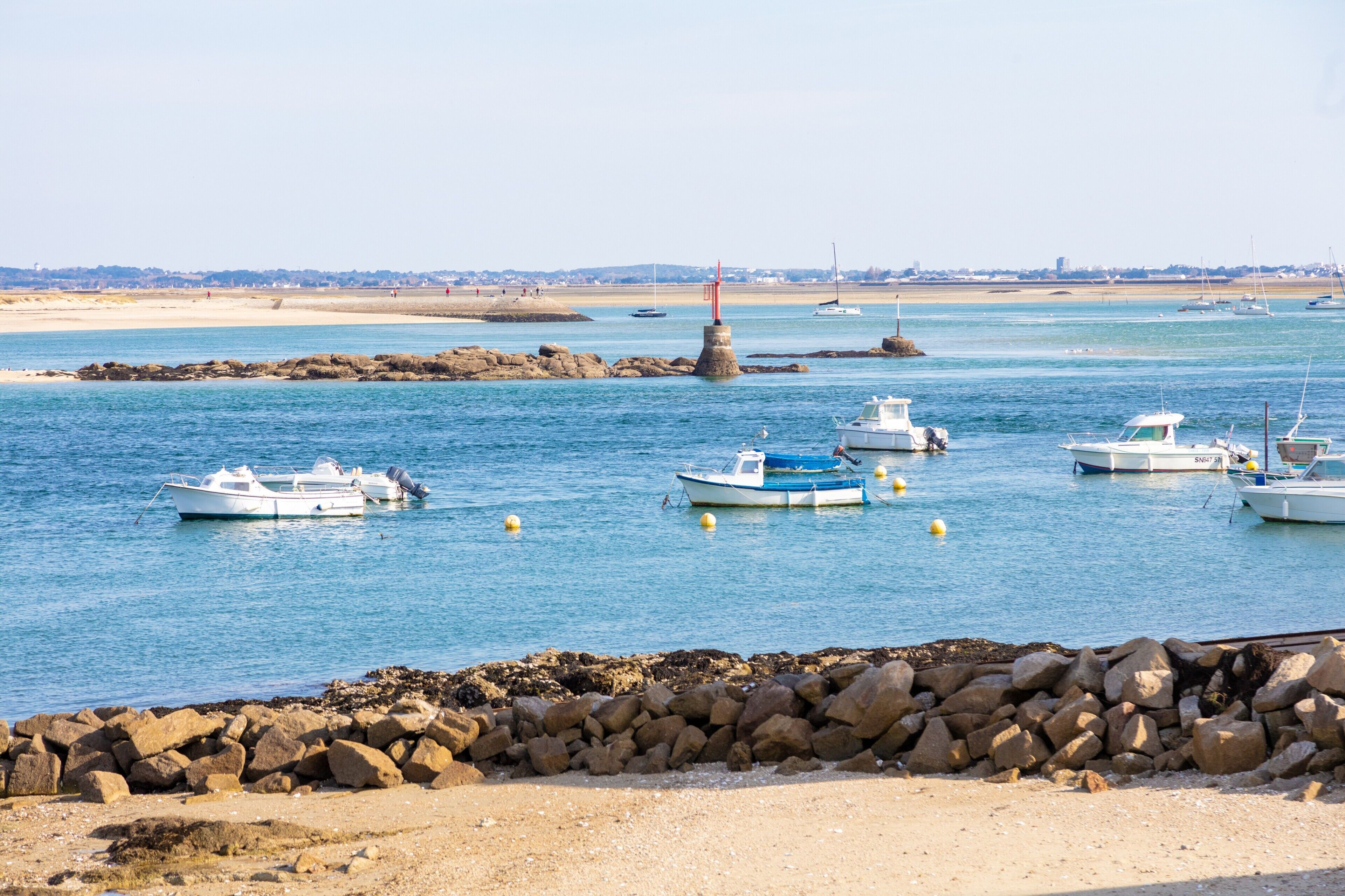 A coastal marina with boats docked, a lighthouse, and a rocky shoreline.