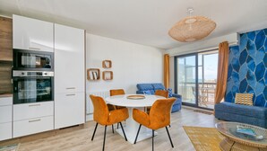A modern kitchen with built-in appliances, a dining area with orange chairs, a blue sofa, and a large window. - Apartment 'Vue Mer 20m De La Plage' with Private Terrace (Le Croisic)