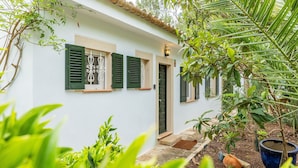 Un bâtiment blanc avec des volets verts, un toit en tuiles et un petit jardin agrémenté de plantes en pot.