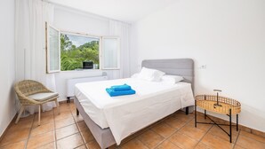 Une chambre à coucher comprenant un lit, une chaise, une table de chevet et une fenêtre donnant sur un paysage verdoyant.