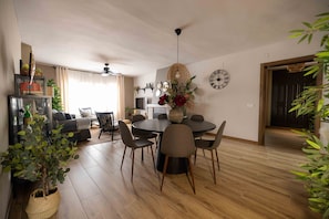 A dining area with a round table, chairs, a vase with flowers, a clock, and a ceiling fan.