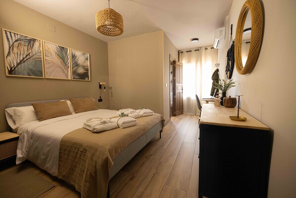 A bedroom with a bed, bedside tables, a desk, a mirror, and artwork on the wall.