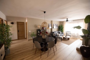A modern living room with a dining area, wooden flooring, and a ceiling fan.