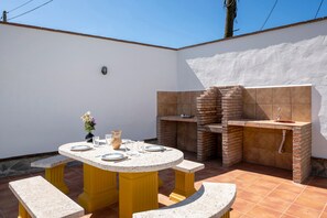Une terrasse extérieure avec une table ronde, des bancs, un four en briques et un évier.