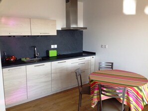 A compact kitchen with a black countertop, a green toaster, and a striped tablecloth-covered table. - L'escale, apartment for 4 guests (Les Sables-d'Olonne)