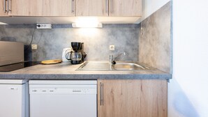 A kitchen with wooden cabinets, a built-in dishwasher, a coffee maker, and a sink. - Apartment 'La Croix Du Sud' with Mountain View and Balcony (Valmeinier)