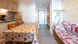 A compact room with a kitchenette, a dining table, a sofa, and a hallway leading to another room. - Apartment 'La Croix Du Sud' with Mountain View and Balcony (Valmeinier)