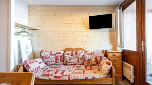 A wooden-paneled room with a bed, a television mounted on the wall, and a window with curtains. - Apartment 'La Croix Du Sud' with Mountain View and Balcony (Valmeinier)
