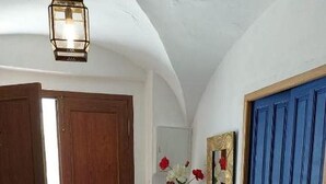 Un couloir doté d’un sol carrelé, d’une porte en bois, d’une porte bleue, d’une console blanche ornée d’un vase de fleurs et d’un luminaire suspendu.