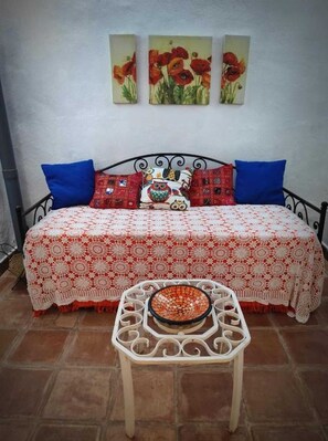 A bed with a patterned bedspread, two blue pillows, and a decorative owl pillow. There are three framed paintings on the wall above the bed.