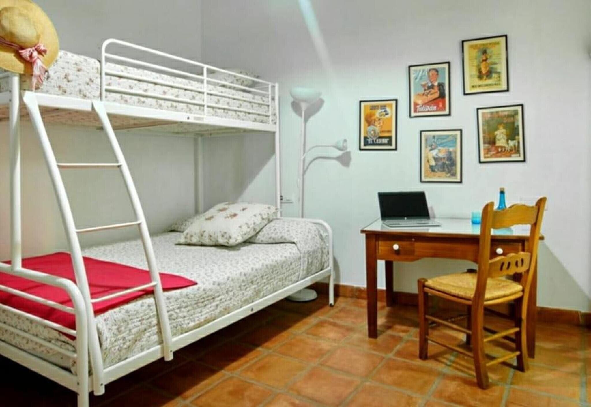 A bunk bed with a desk and chair, a lamp, and several framed pictures on the wall.