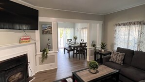A living room with a fireplace, a flat-screen TV, a dining area, and a sofa. - Peaceful Onset Beach Home. 5 Bedrooms, Wareham MA (Wareham)