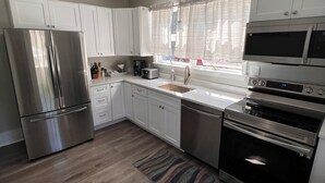 A modern kitchen with white cabinets, stainless steel appliances, and a window with curtains. - Peaceful Onset Beach Home. 5 Bedrooms, Wareham MA (Wareham)