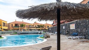 Une piscine avec des chaises longues et un parasol en chaume.