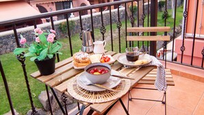 Un balcon avec une table préparée pour le petit-déjeuner, comprenant des viennoiseries, des fruits et une cafetière.