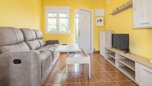 Una sala de estar con sofá, una mesa de centro, televisor sobre un mueble y puerta que da al exterior.