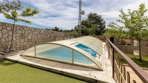 Una piscina con cerramiento de vidrio, rodeada por un muro de piedra y una valla metálica.