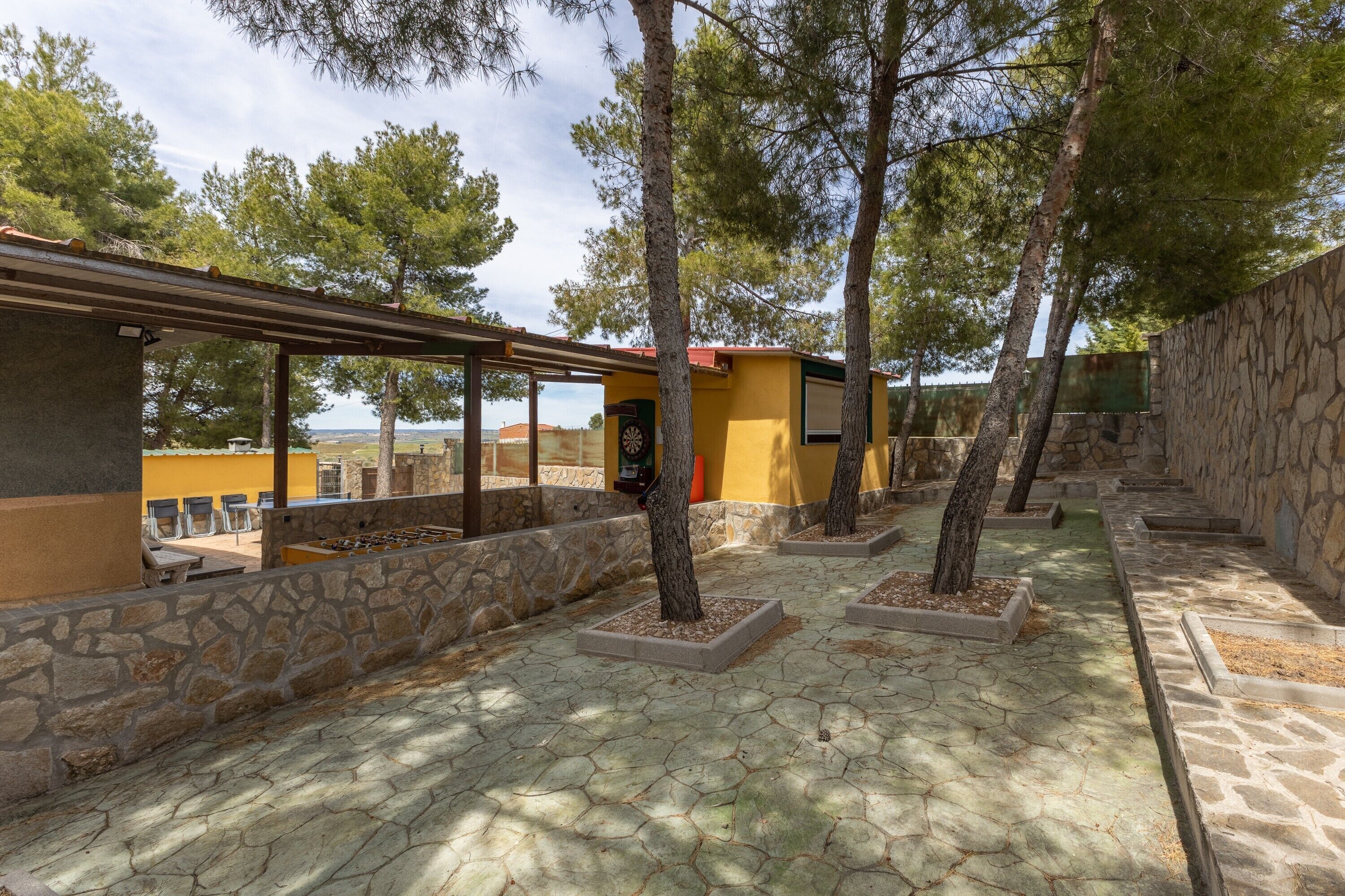 Un patio con suelo de piedra, árboles y un edificio amarillo con techo rojo.