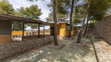 Un patio con suelo de piedra, árboles y un edificio amarillo con techo rojo.