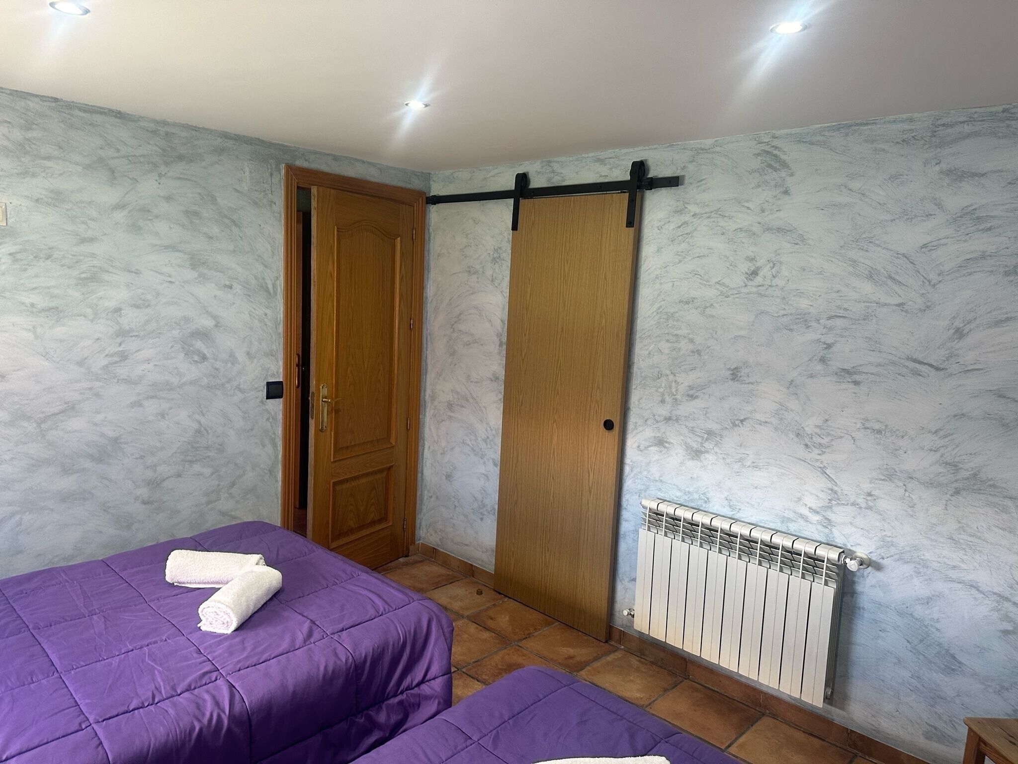 Una habitación con dos camas, una puerta de madera, un radiador y una lámpara en el techo.