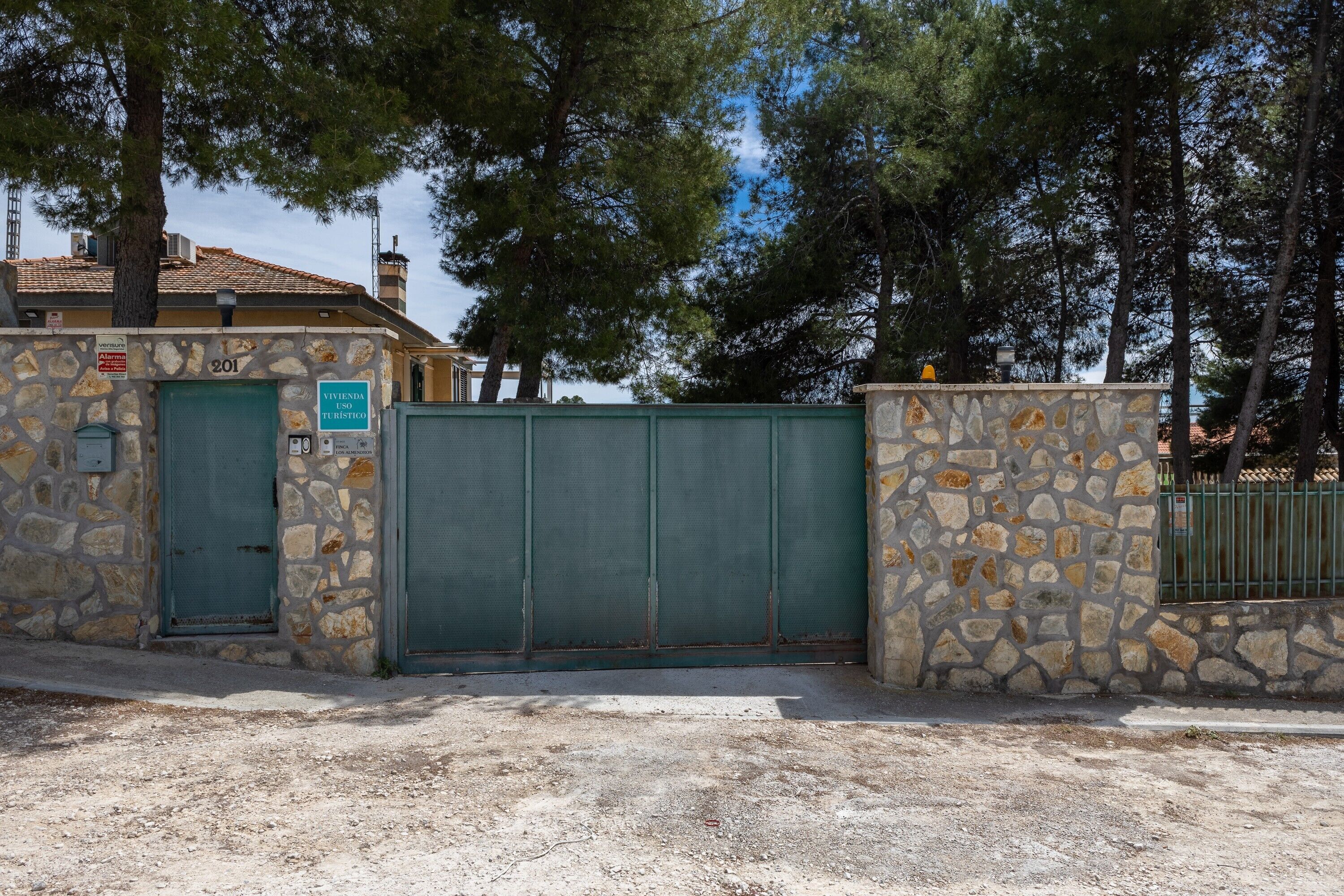 Un edificio de piedra con un portón verde, un letrero que indica 'Vivenda Turismo' y el número '201' en la pared.
