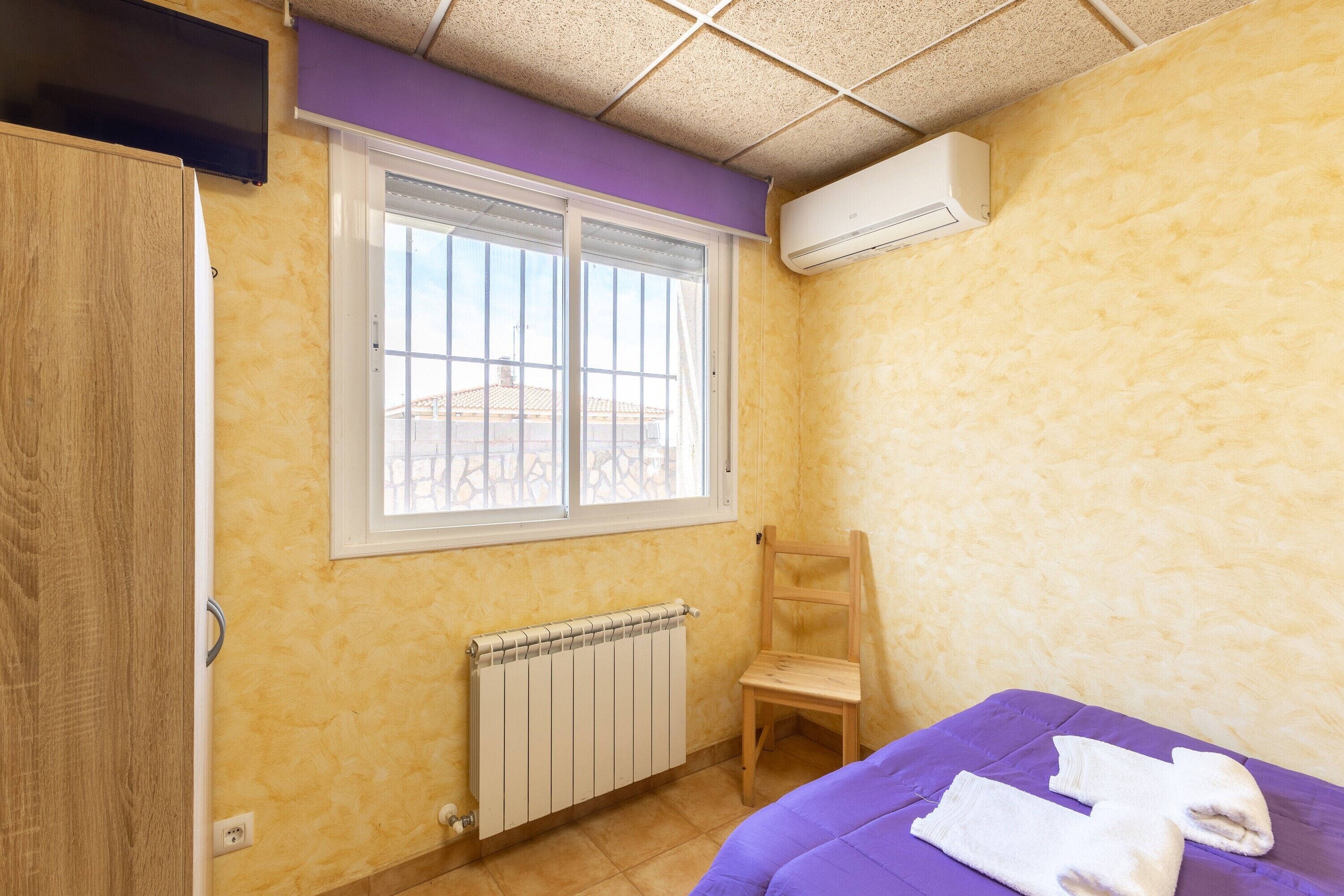 A room with a window, radiator, wooden chair, and a bed with towels.