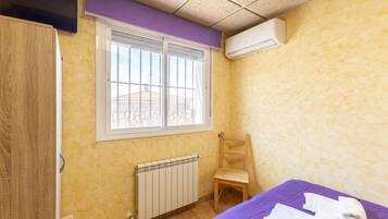 A room with a window, radiator, wooden chair, and a bed with towels.