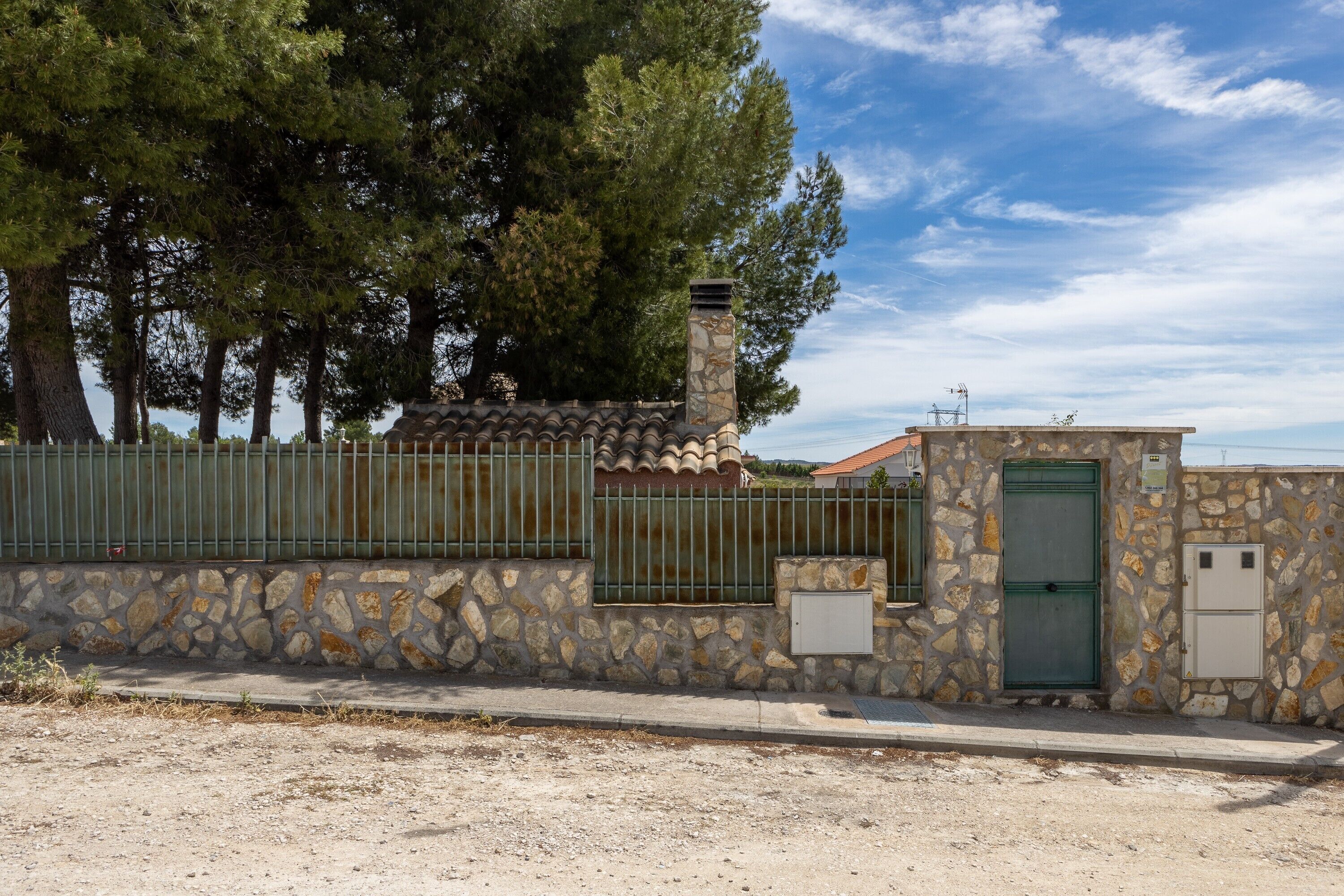 Un edificio de piedra con puerta verde, cerca metálica y chimenea de piedra.