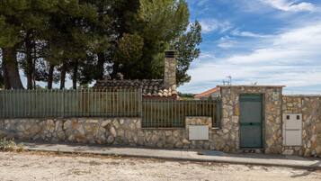 Un edificio de piedra con puerta verde, cerca metálica y chimenea de piedra.
