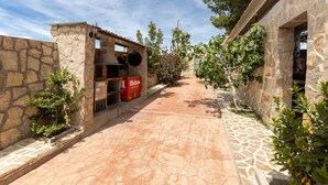 Un chemin de pierre mène à un bâtiment dont la façade est également en pierre, où l’on aperçoit un réfrigérateur rouge de la marque Mahou et une cloche.
