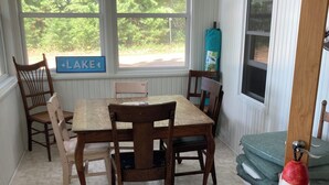 Un coin repas avec une table et des chaises en bois, une enseigne indiquant « LAC », et une vue sur les arbres à travers de grandes fenêtres.