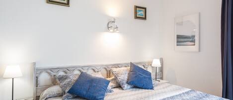 A bedroom with a bed, two bedside lamps, a wall-mounted light, and two framed pictures.