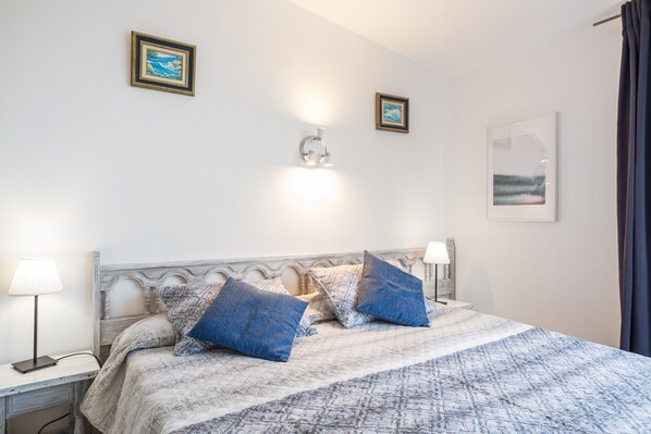A bedroom with a bed, two bedside lamps, a wall-mounted light, and two framed pictures.