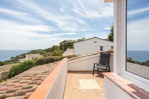 A balcony with a chair, a tiled floor, and a view of the sea and distant buildings.