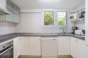 A modern kitchen with white cabinets, a built-in dishwasher, a double sink, and a window with a view of greenery.